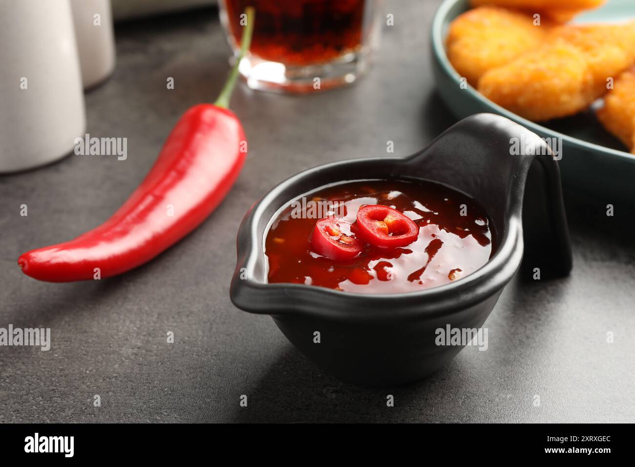 Hot chili sauce in gravy boat on grey textured table, closeup Stock Photo