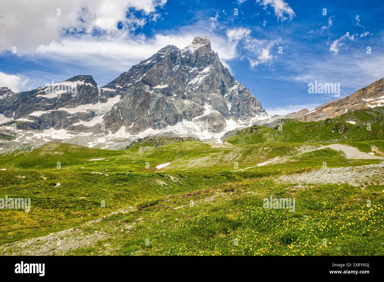 panoramic view of the matterhorn from the italian side with green meadows and yellow  flowers and sunny cloudy sky Stock Photo