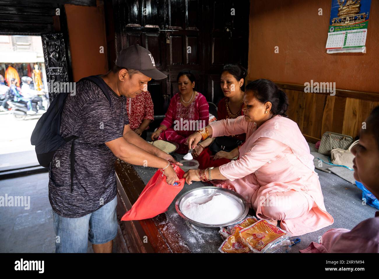 Lalitpur, Nepal. 12th Aug, 2024. A Buddhist distributes an offering during the Pancha Dan festival in Lalitpur, Nepal, on Aug. 12, 2024. Pancha Dan, the festival of five summer gifts, is observed by the Buddhists by giving away five elements including wheat grains, rice grains, salt, money and fruit. Credit: Hari Maharjan/Xinhua/Alamy Live News Stock Photo