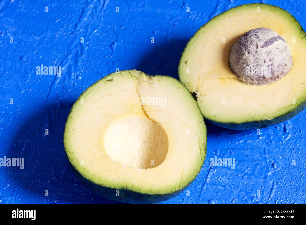 Two avocado halves on a blue background. Stock Photo