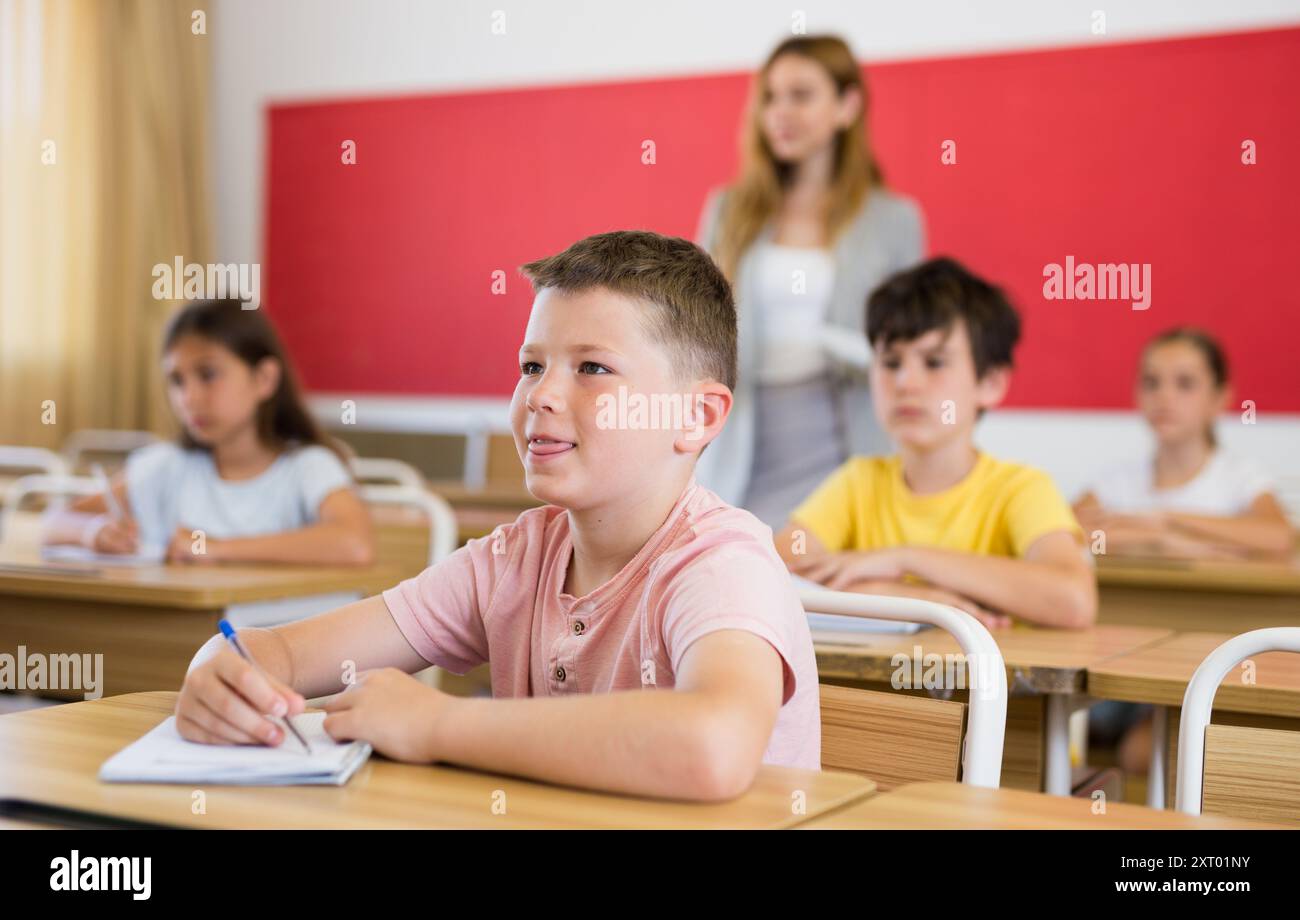 Smiling tween schoolboy sitting in classroom during lesson Stock Photo ...