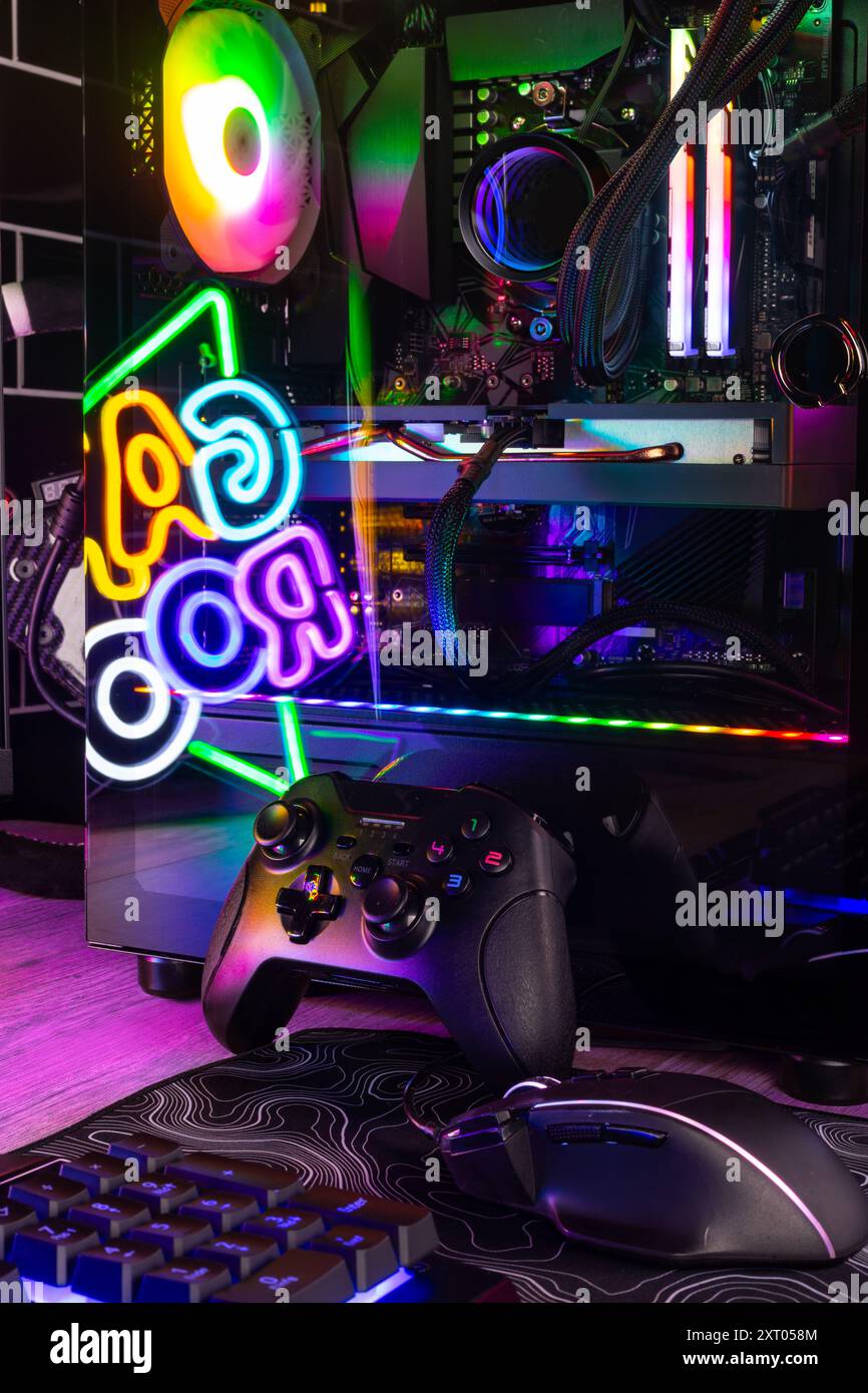 Vertical shot of colorful gaming pc desk with bright raimbow led computer gamepad mouse keyboard and steering wheel. esports video games concept  back Stock Photo