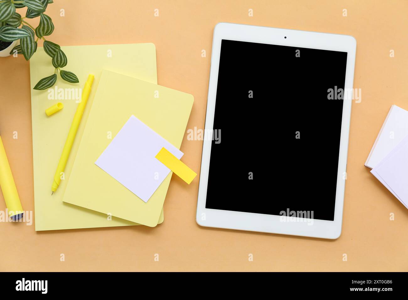 Tablet with notebooks and sticky notes on orange background Stock Photo