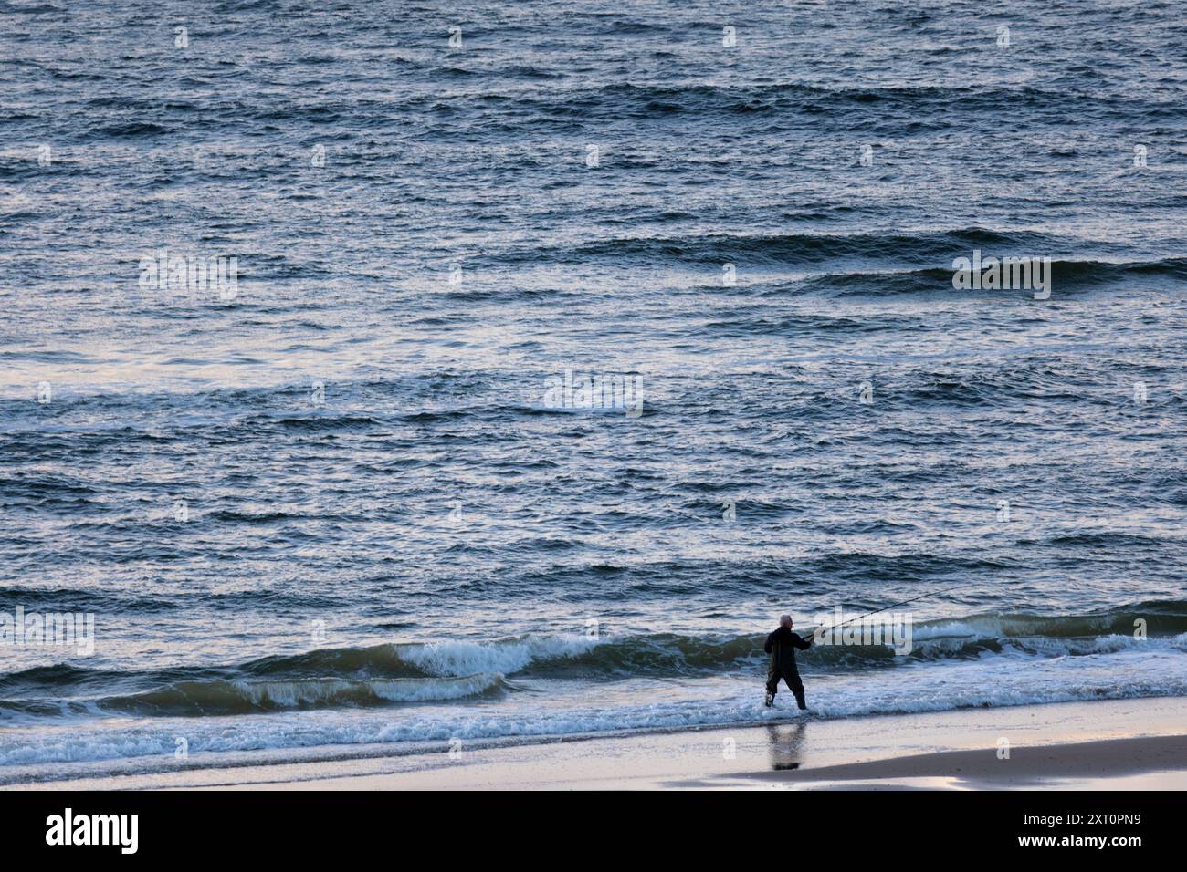Silhouette of a fisherman standing on the beach in front of sea in dawn ...