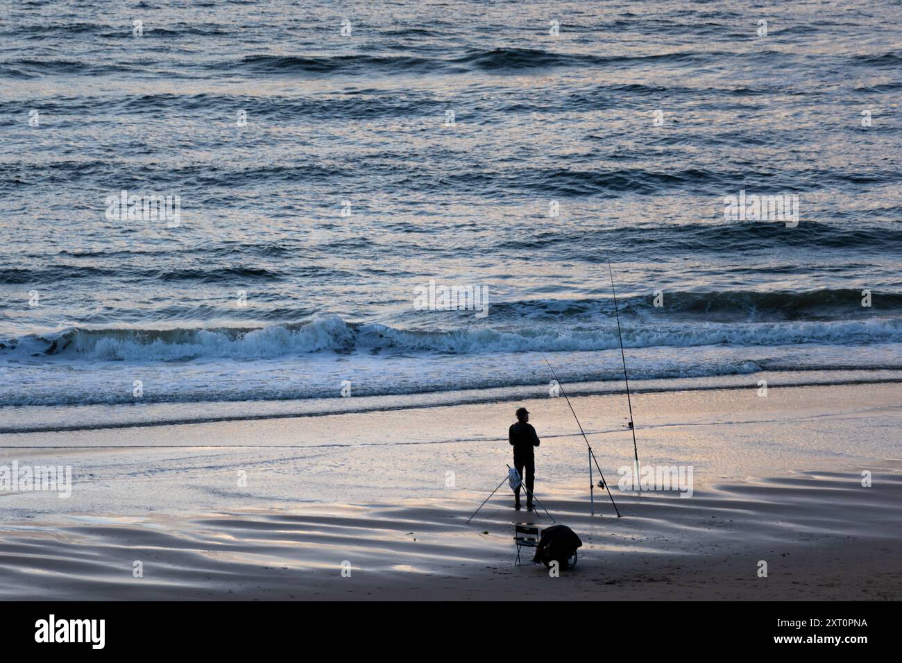 Silhouette of a fisherman standing on the beach in front of sea in dawn ...