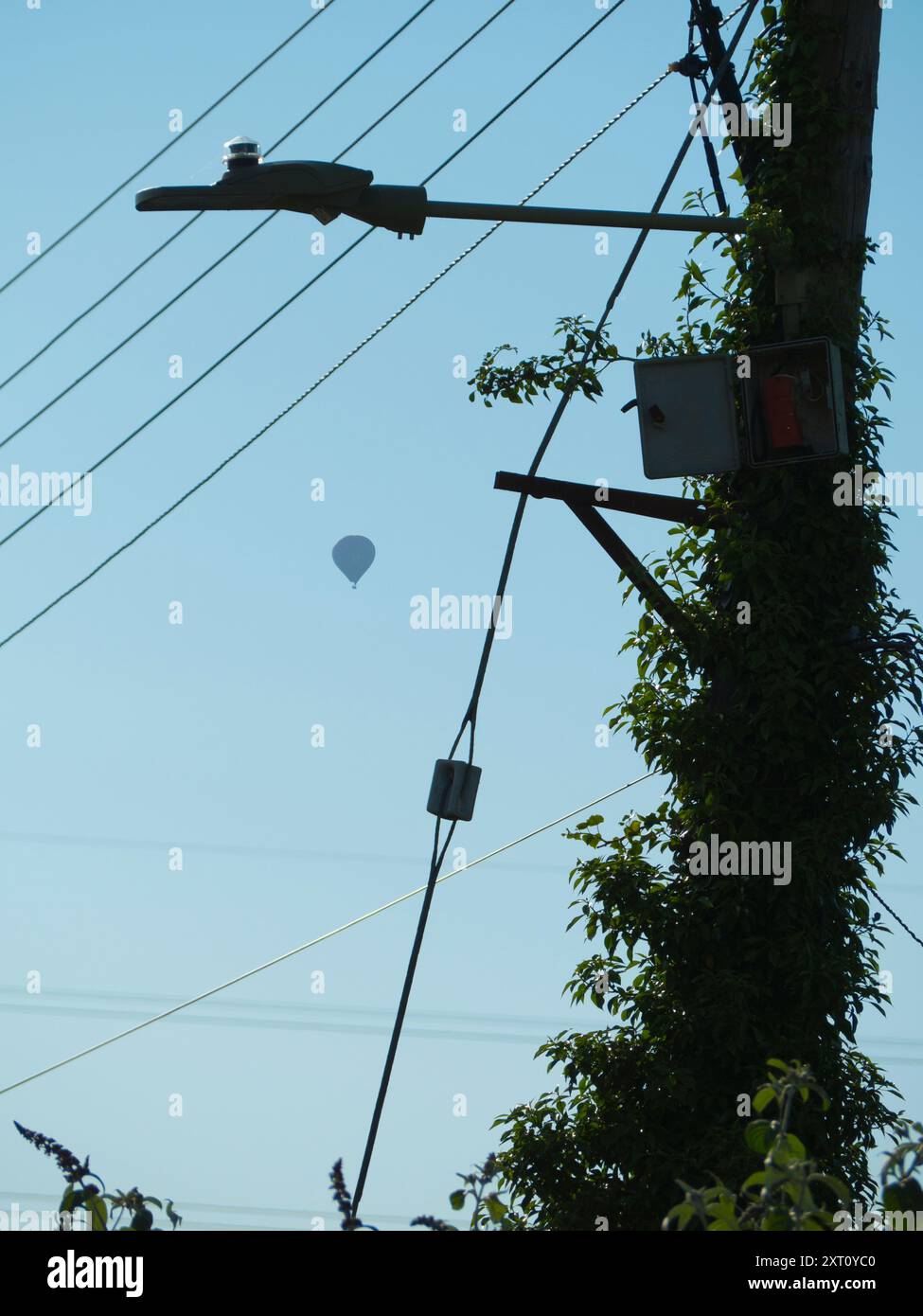 I walk around my home village of Radley every day, and I always carry a camera. It's surprising what you see sometimes, even on walks you've done hundreds of times and think you know backwards. Here we see a pole carrying a street light, telephone wires and assorted cables on my walk through Lower Radley to the River Thames, with a hot air balloon floating serenely above. Stock Photo