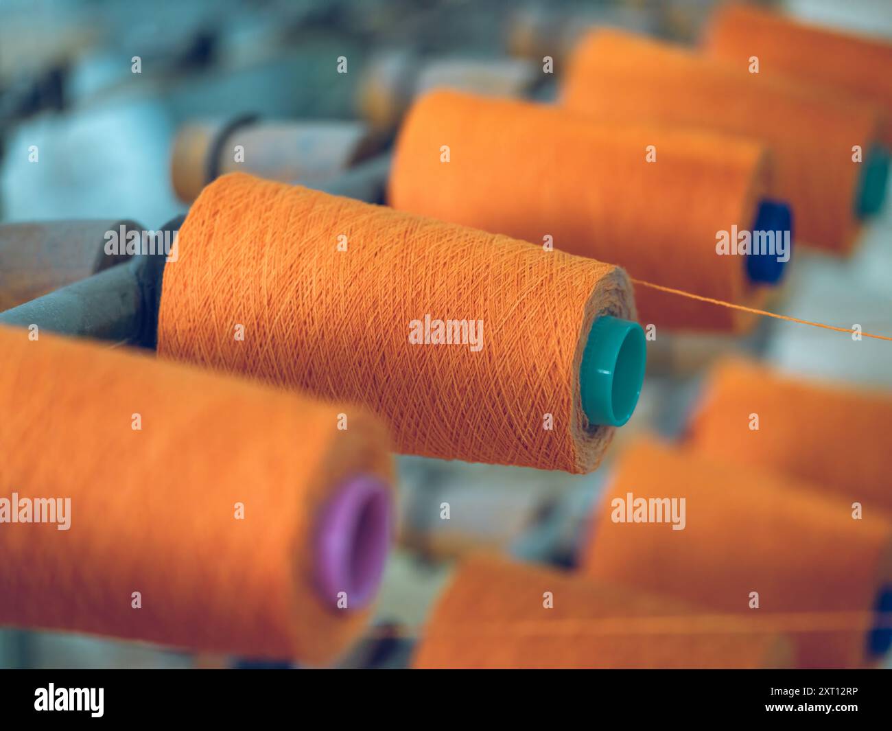 Rows of orange yarn spools mounted on machines in a textile factory ...