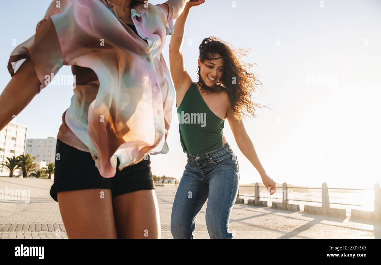 Two young women dancing on the boardwalk, embodying vitality and joy, enjoying their twenties on a sunny day. Stock Photo