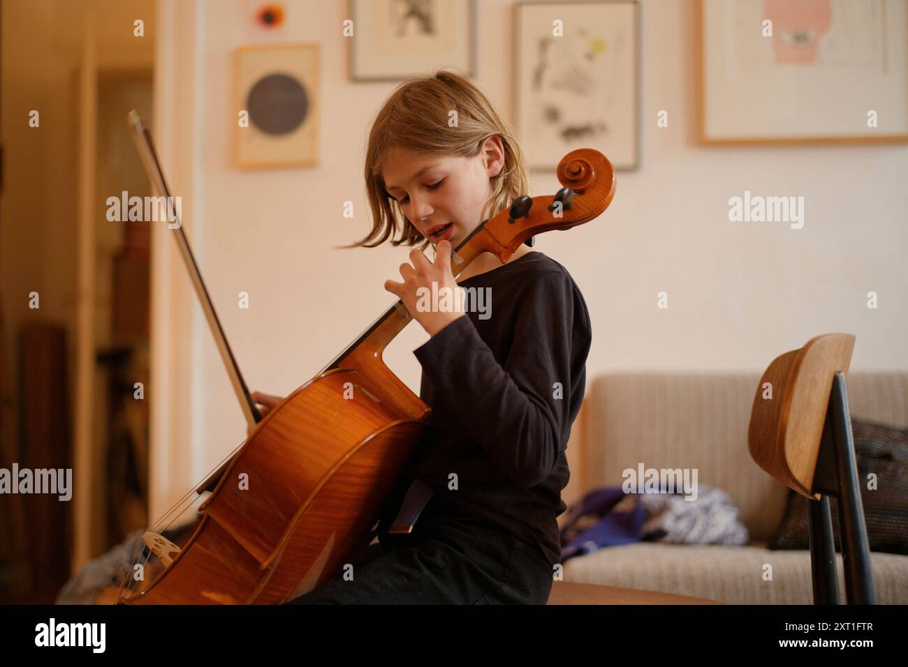 Young child practices playing cello in a cozy home environment with artwork on the wall. bola02488 Copyright: xConnectxImagesx Stock Photo