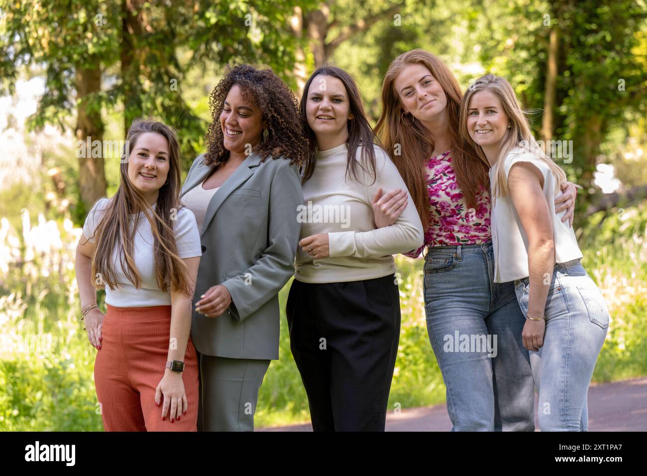 Group of five smiling women posing together in a sunny park setting ...