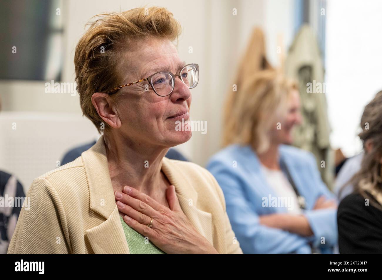 A woman with glasses wearing a beige jacket is touching her chest with a hand, showing an expression of gratitude or relief. panc05782 Copyright: xCon Stock Photo