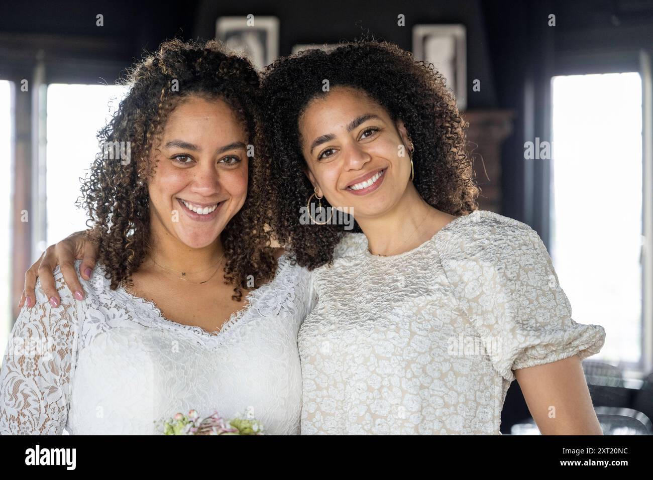 Two smiling women with curly hair embracing each other in a room with natural light. panc05813 Copyright: xConnectxImagesx Stock Photo