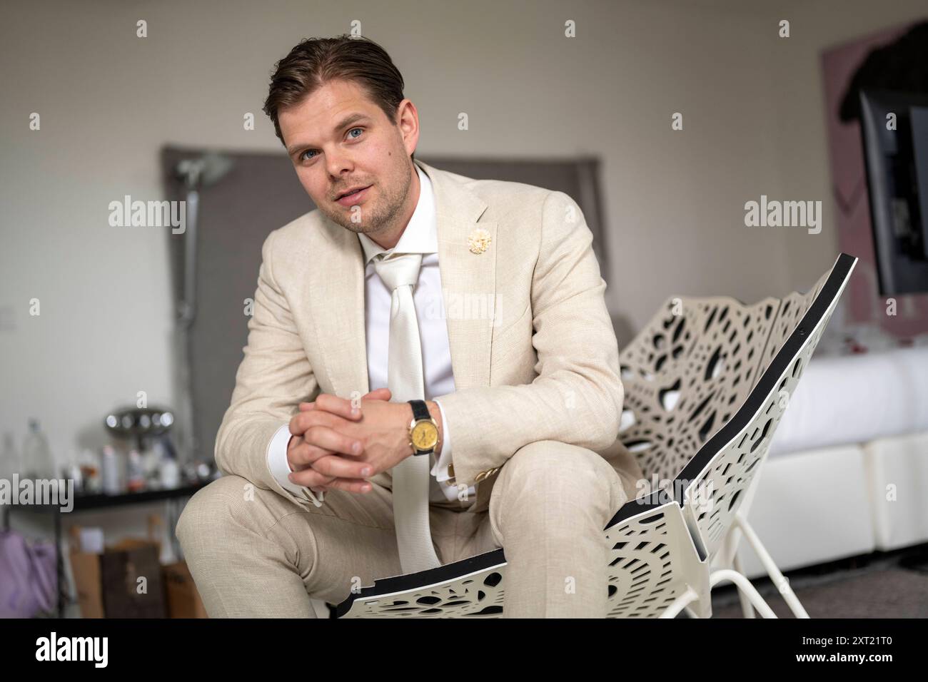 Well-dressed man in a beige suit sitting on a modern chair indoors, confidently looking at the camera with a slight smile. panc05941 Copyright: xConne Stock Photo