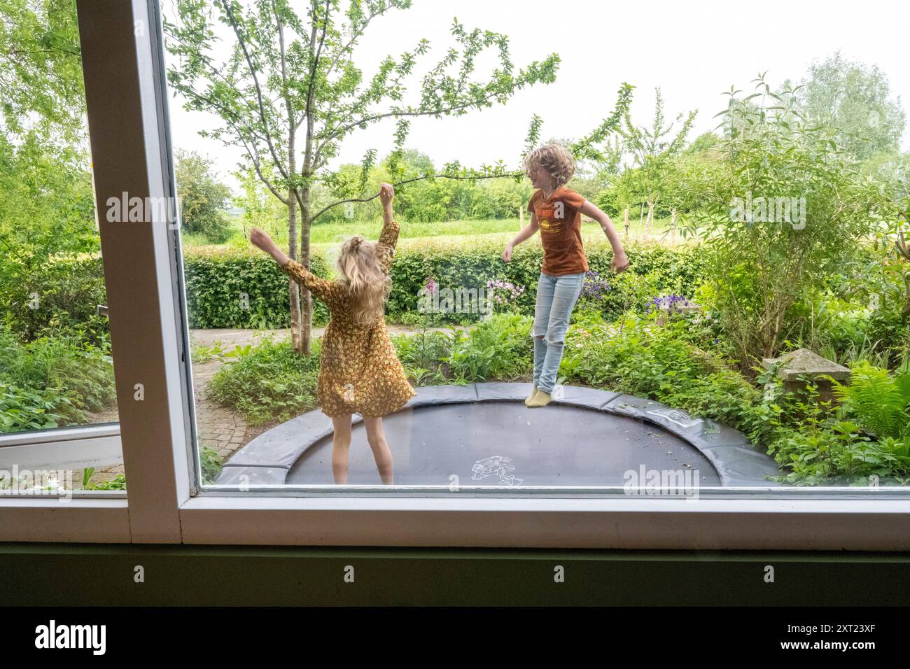 Two children are joyfully jumping on an outdoor trampoline in a lush ...