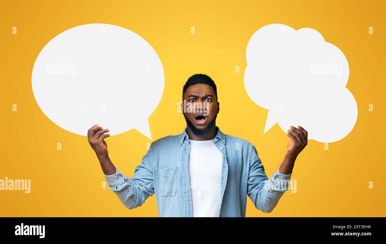 Confused black guy holding two speech bubbles on yellow background Stock Photo