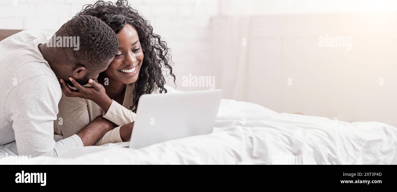 Cheeful african american couple relaxing on bed with laptop Stock Photo ...