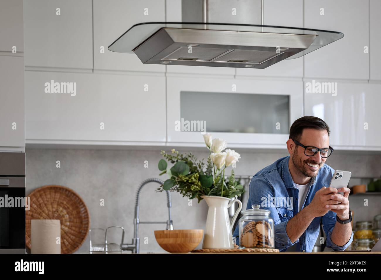 Smiling male entrepreneur online messaging over smart phone while leaning on kitchen counter Stock Photo