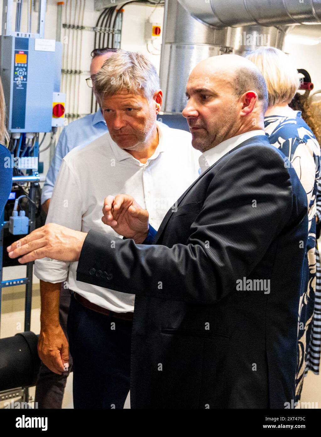 Norderstedt, Germany. 13th Aug, 2024. Federal Minister of Economics Robert  Habeck (Alliance 90/The Greens, l) has a large heat pump explained to him  by Nico Schellmann, Plant Manager Energy at Stadtwerke Norderstedt,