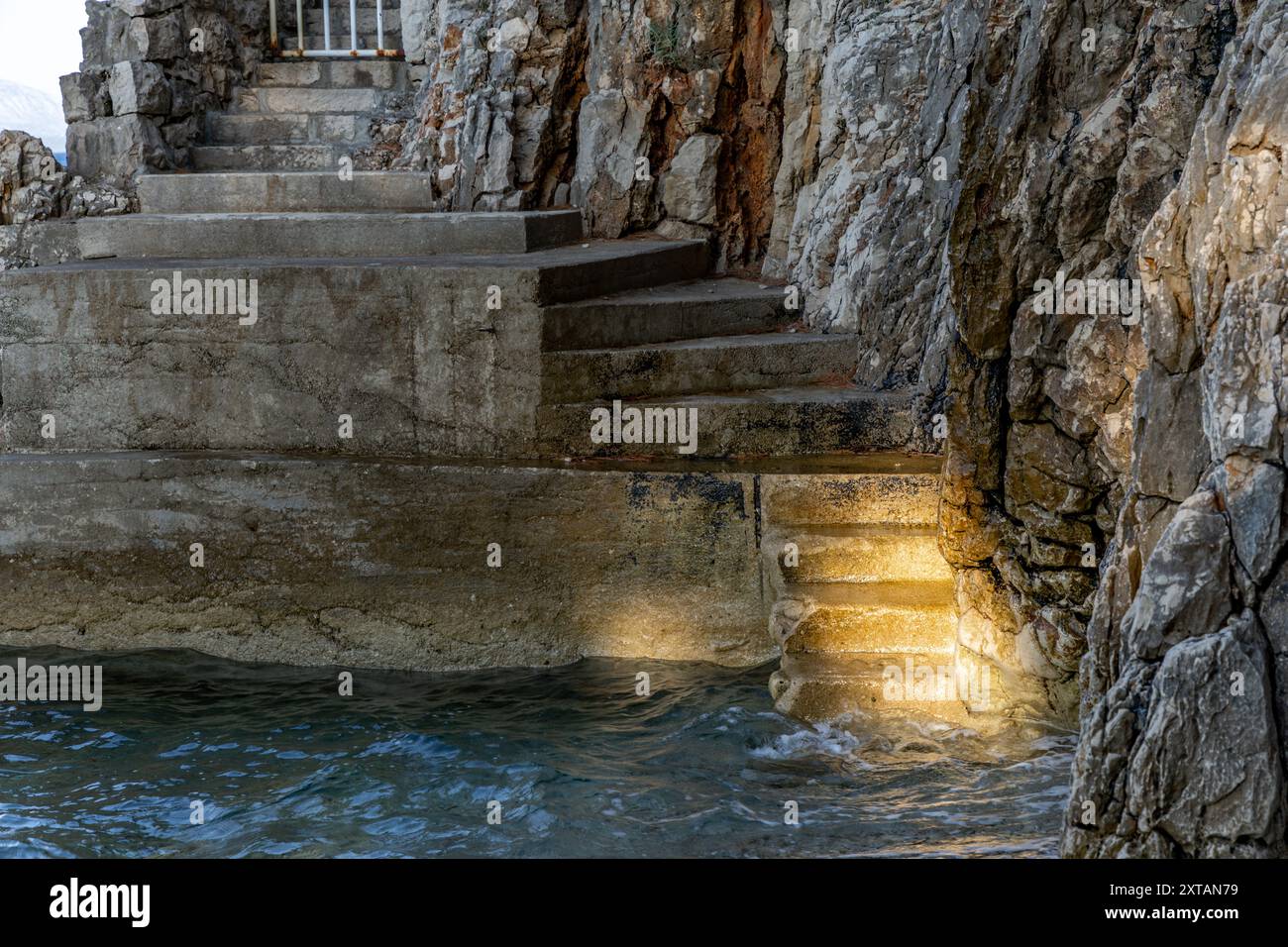 Steep descent down stairs to a rocky beach, Adriatic Sea coast in Croatia, safety railing made of thick fishing rope Stock Photo