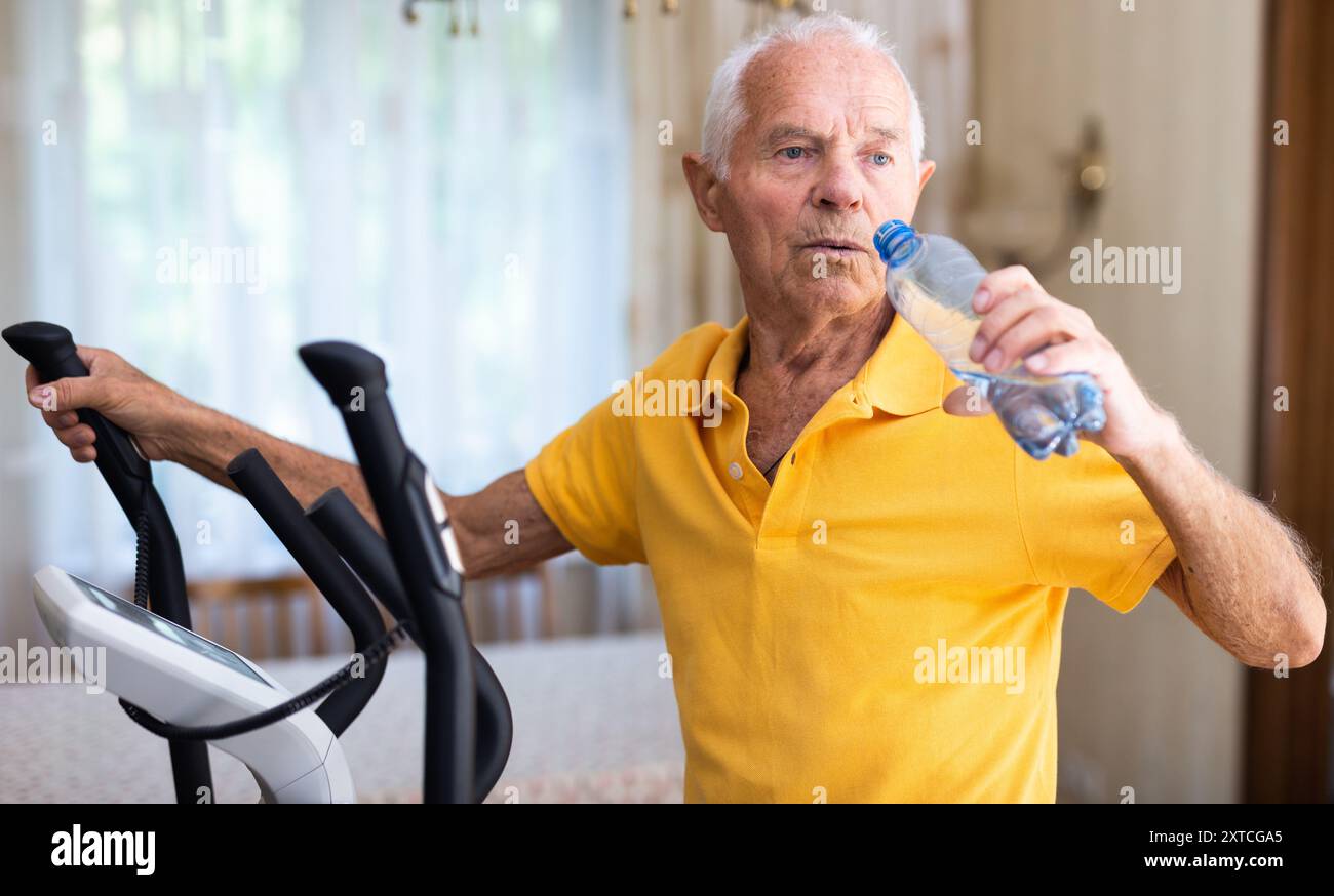 Senior man using elliptical trainer and drinking water Stock Photo