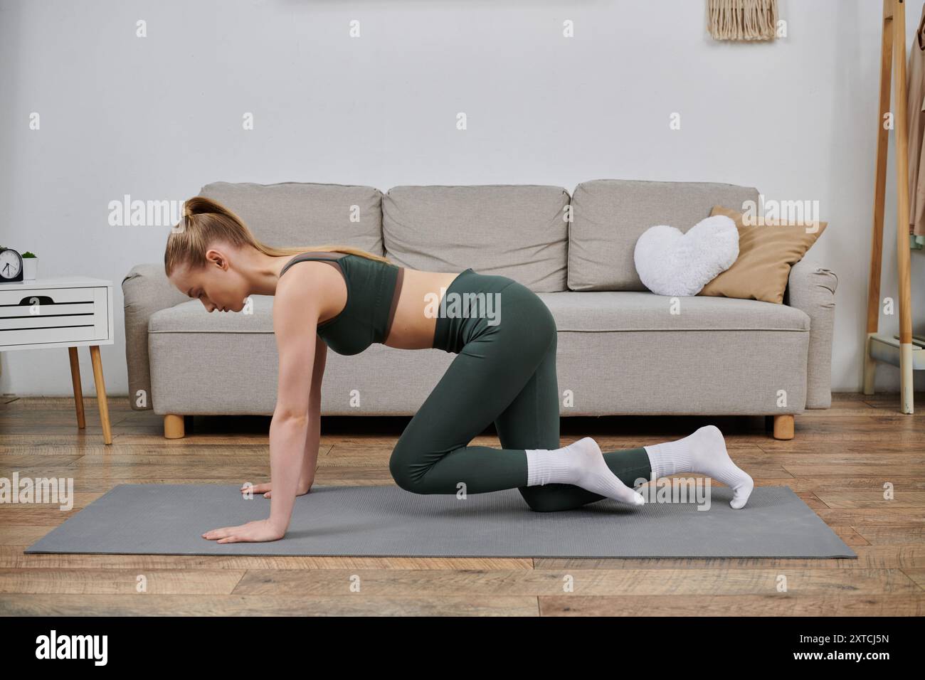 A young woman in workout attire performs a stretch on a mat in her ...