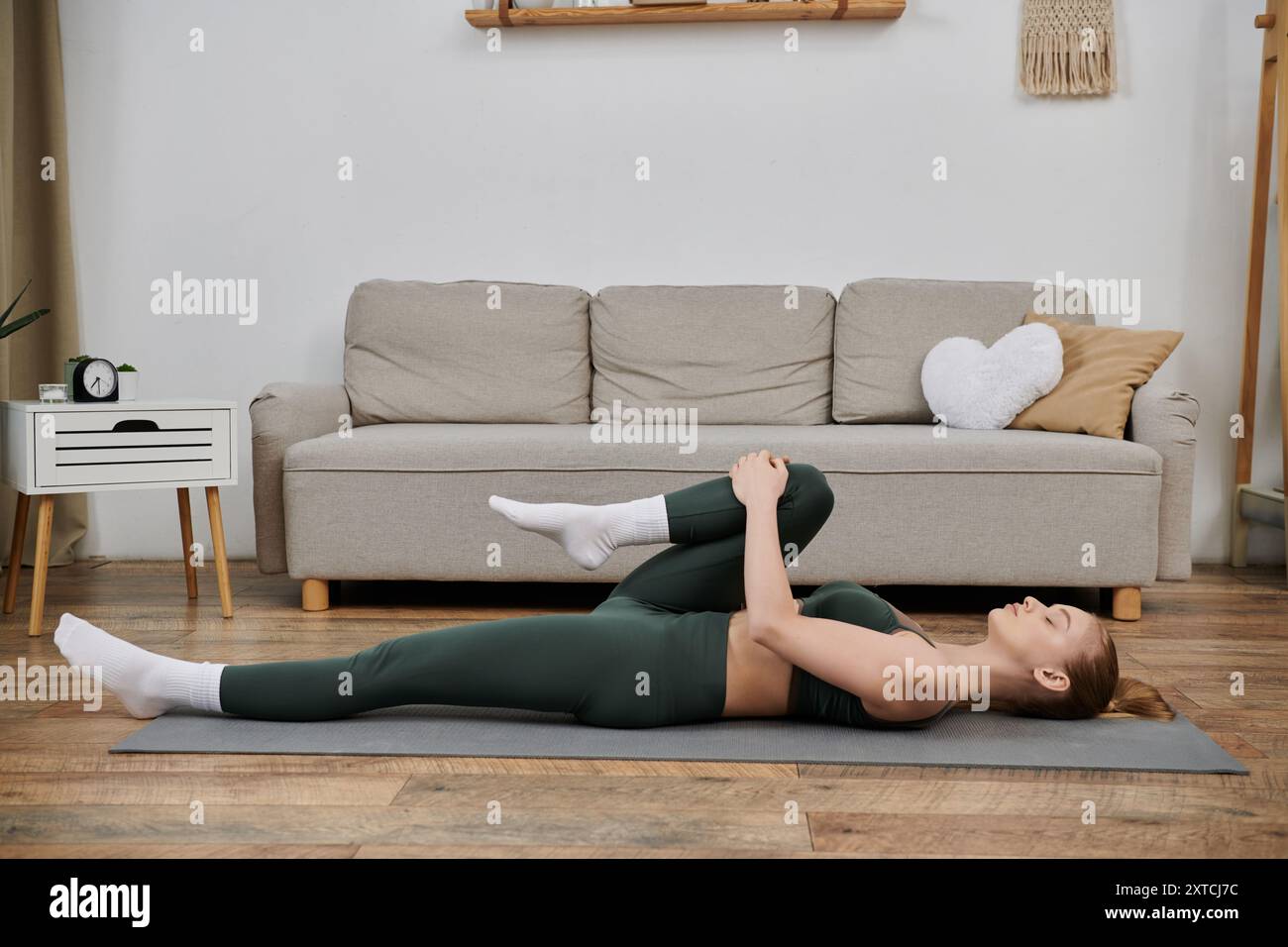 A young woman performs a stretching exercise on a yoga mat in her ...