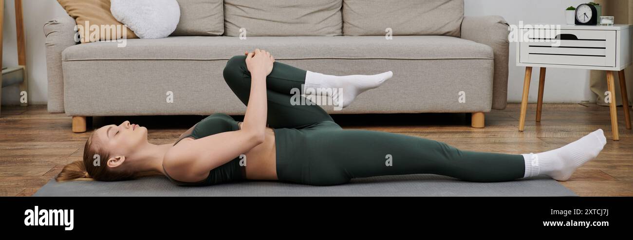 A young woman performs a stretching exercise on a grey mat in her ...
