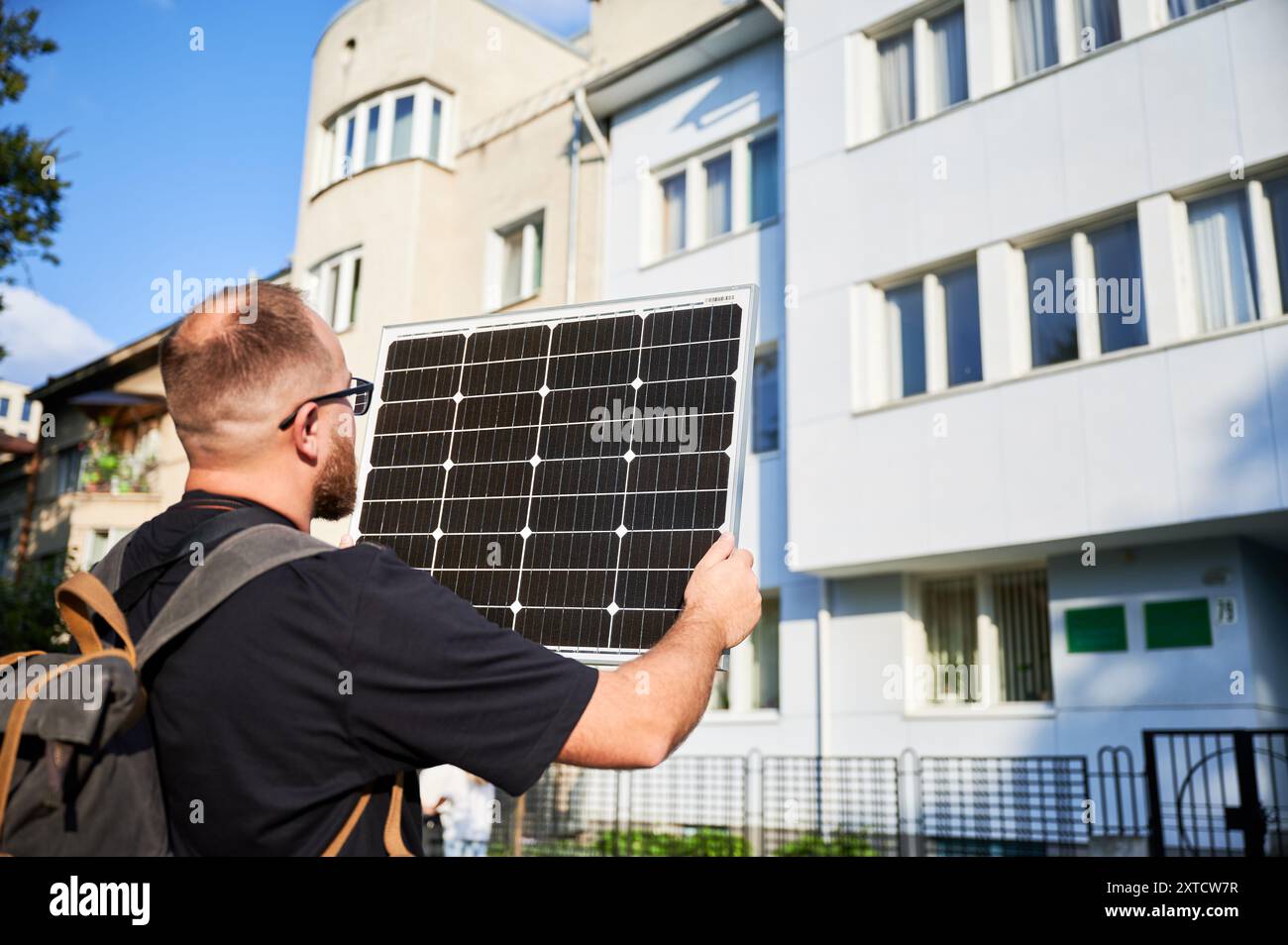 Man holding photovoltaic solar panel in front of historical building. Concept of integration of sustainable renewable energy sources into architecture. Stock Photo