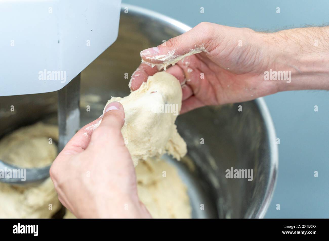 The dough for bread or donuts in the hands of a technologist or baker is checked for readiness and quality against the background of a production planetary mixer. Close-up. Selected focus. High quality photo Stock Photo