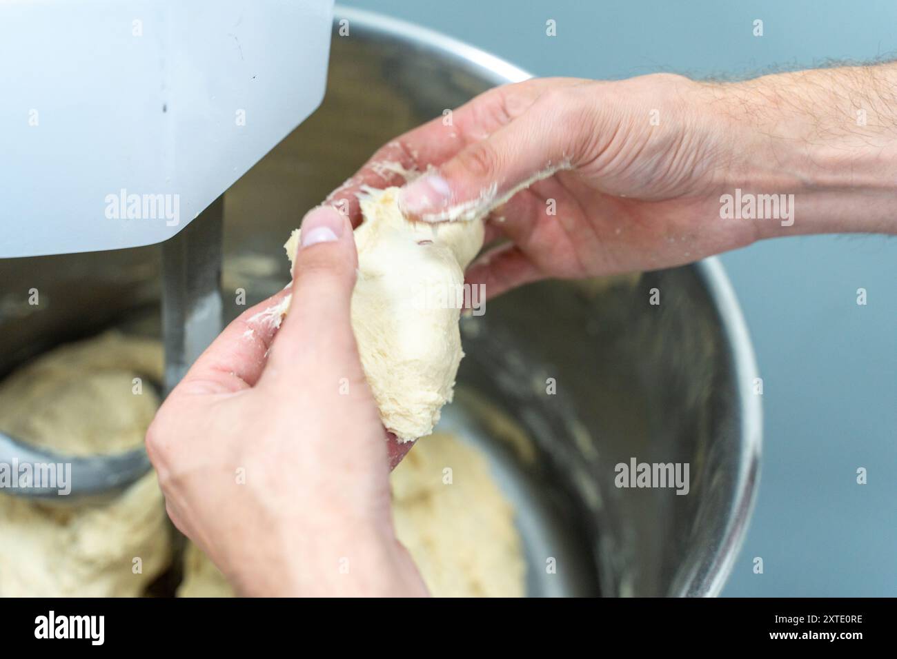 The dough for bread or donuts in the hands of a technologist or baker is checked for readiness and quality against the background of a production planetary mixer. Close-up. Selected focus. High quality photo Stock Photo