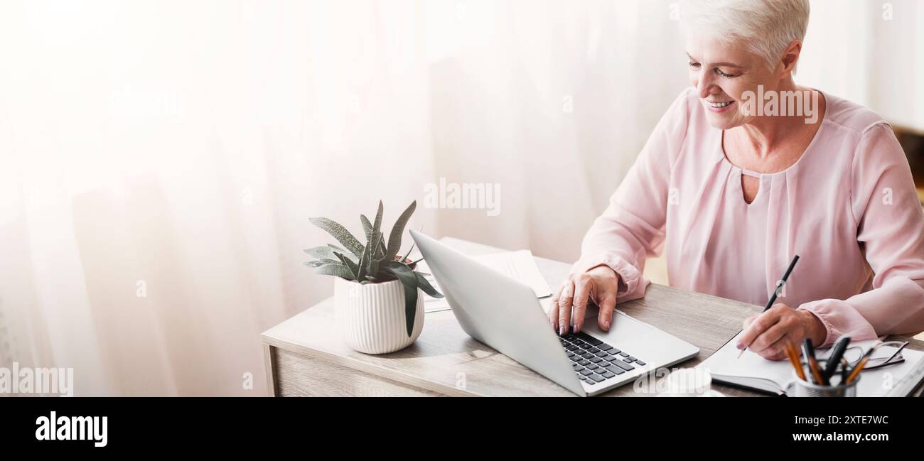 Top view of mature working lady making notes, using laptop Stock Photo