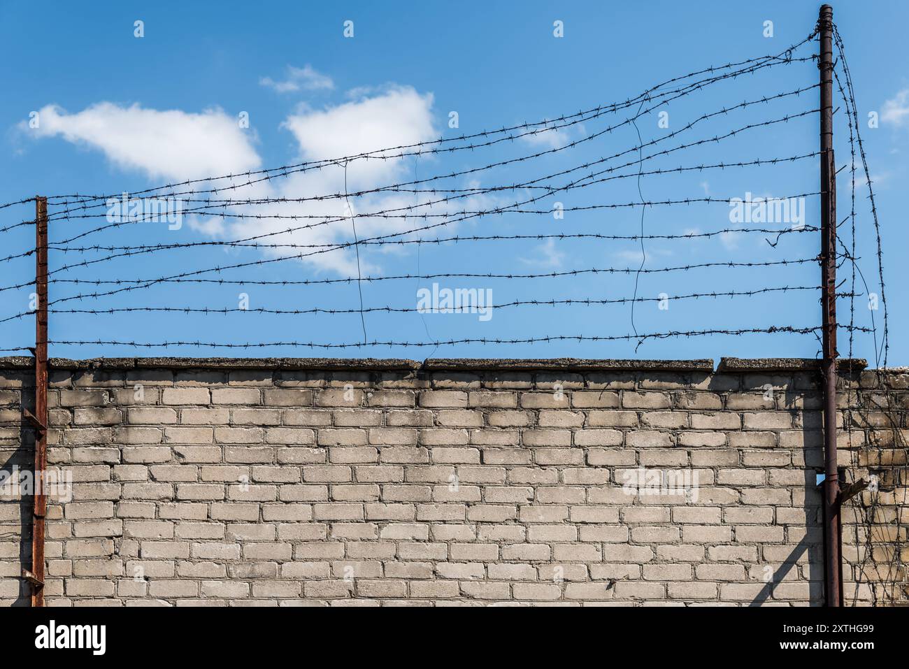 Old Abandoned Prison White Brick Wall With Rusty Metal Barbed Fence In Blue Sky Background Stock Photo