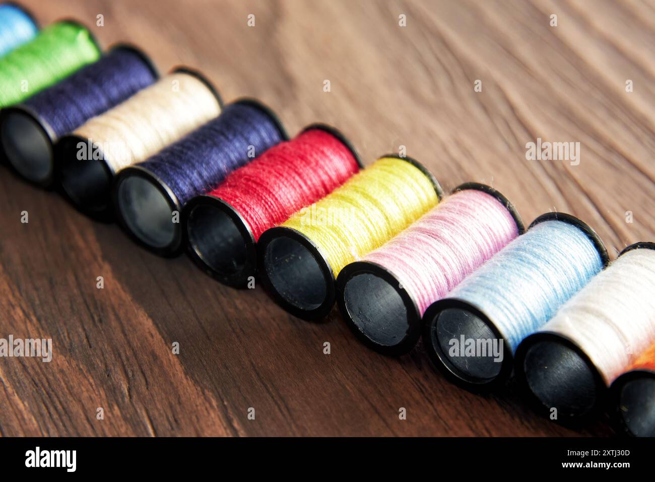 Row of colorful threads on spools are arranged on a wooden surface. Sewing equipment objects Stock Photo
