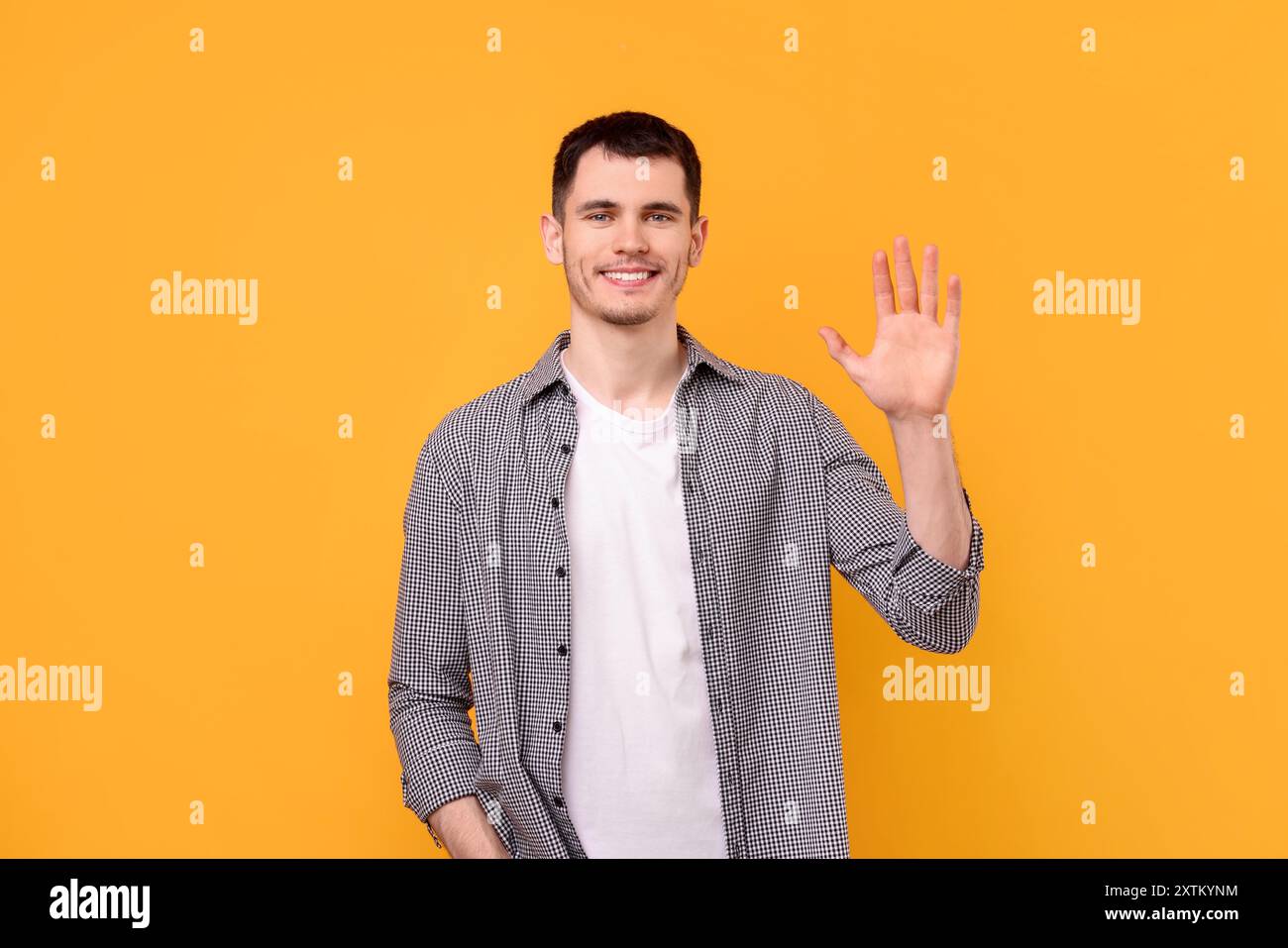 Happy young man waving on orange background Stock Photo