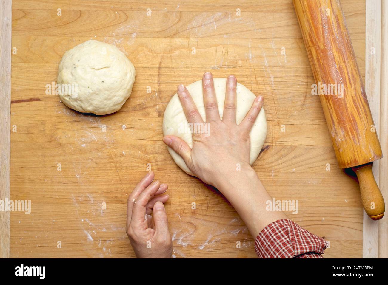 A flatlay photo of patting a small ball of dough down to get it ready to roll out using the rolling pin. Stock Photo