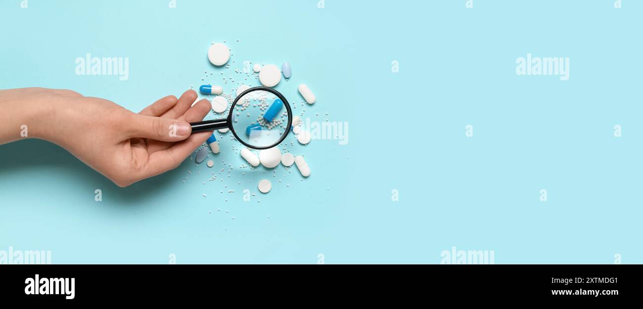 Female hand with magnifier and pills on blue background with space for text Stock Photo