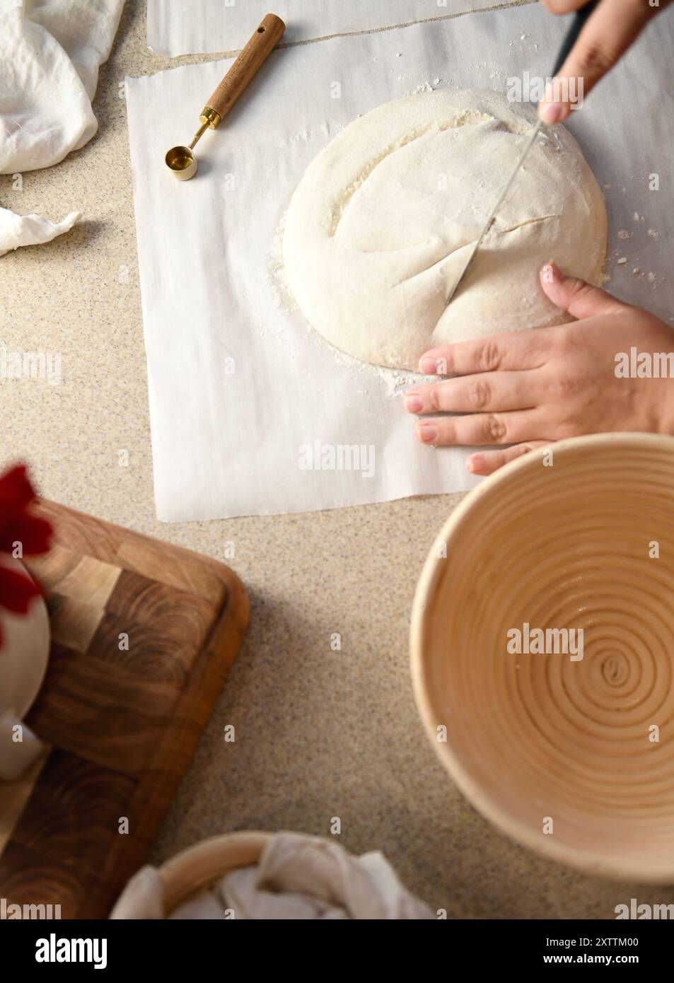 Hands cutting dough with a knife on parchment paper, next to a p Stock Photo