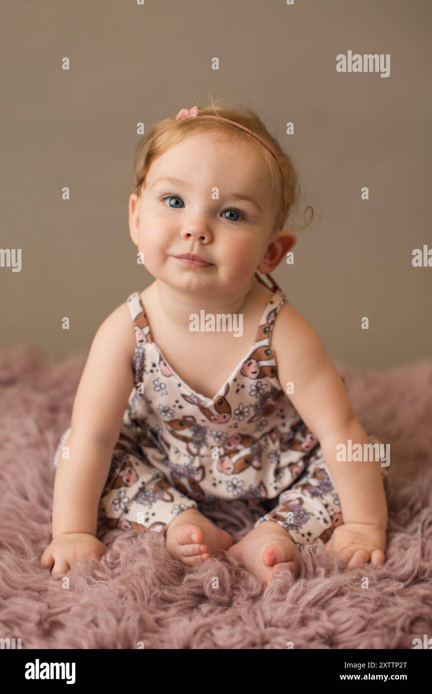 Smiling blue eyed girl in a cow print romper on a pink rug Stock Photo -  Alamy