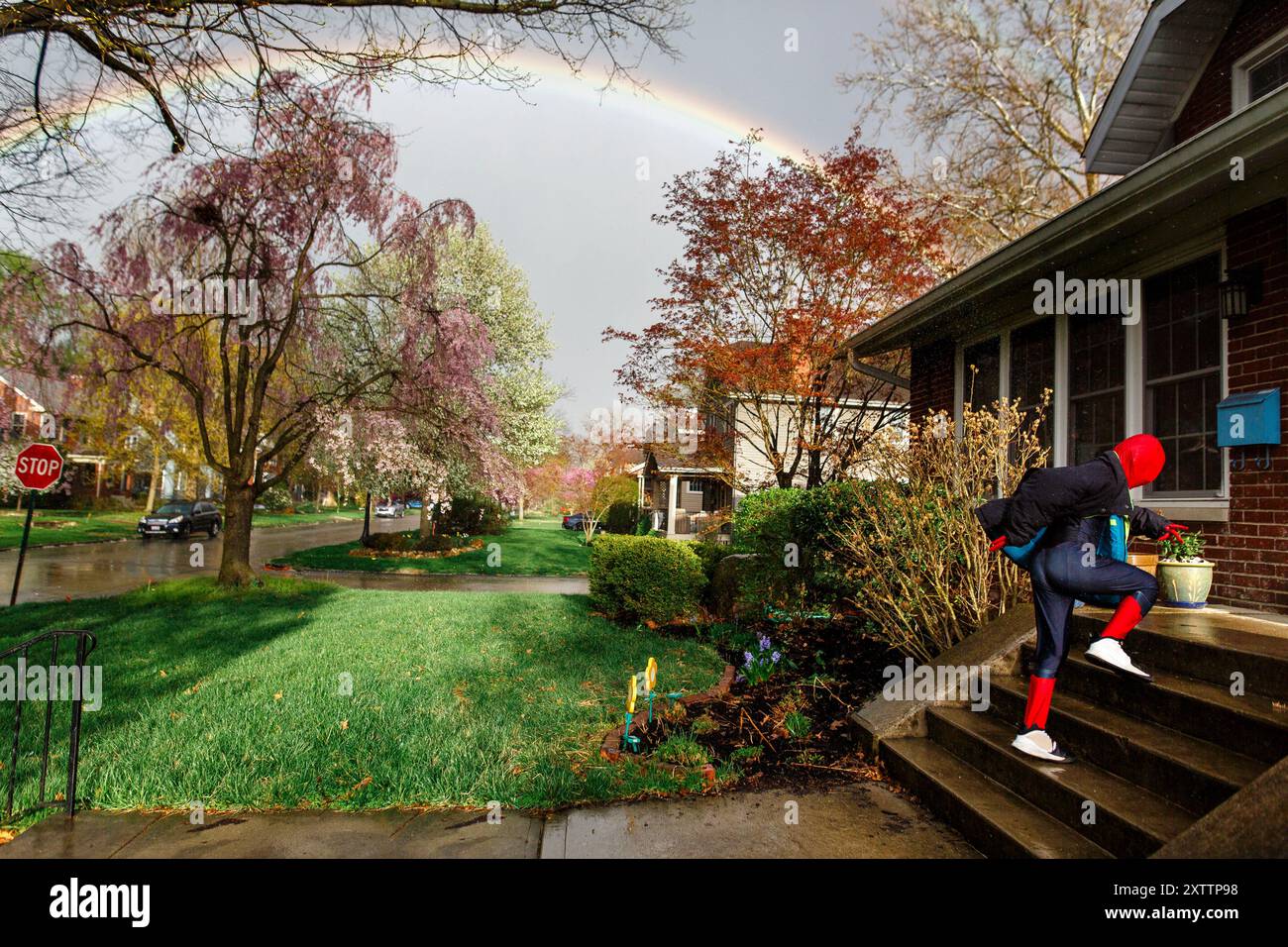 A child in Spiderman costume runs under rainbow Stock Photo