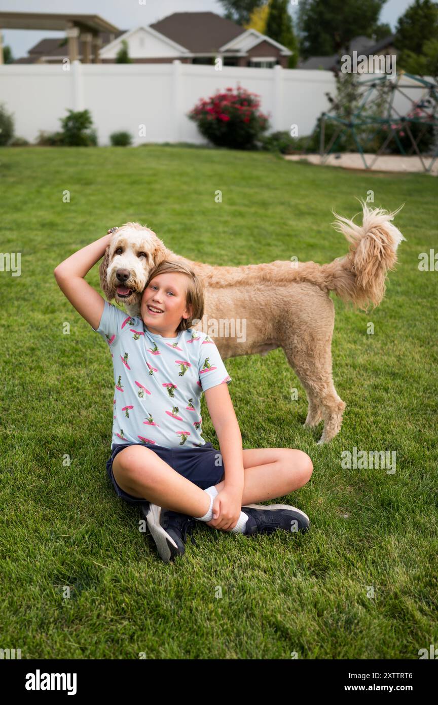 teen boy sitting on the grass in a backyard, hugging a big fluffy dog Stock Photo