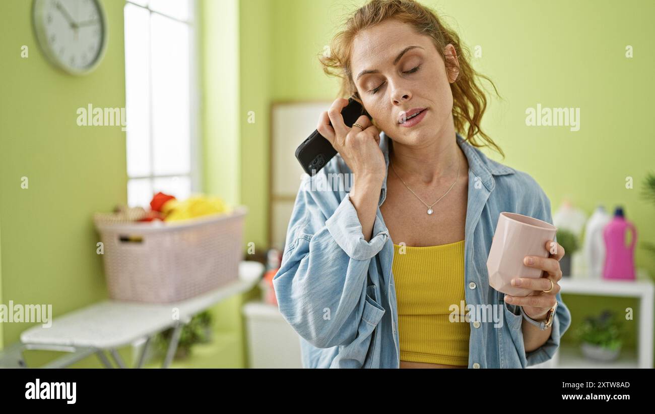 A young woman multitasks with a phone and mug in a home laundry room ...