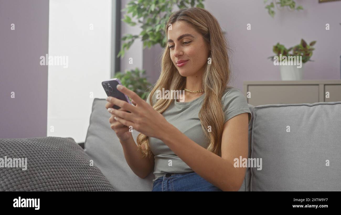 A young woman engages with her smartphone on a couch, conveying leisure in a cozy living room setting. Stock Photo