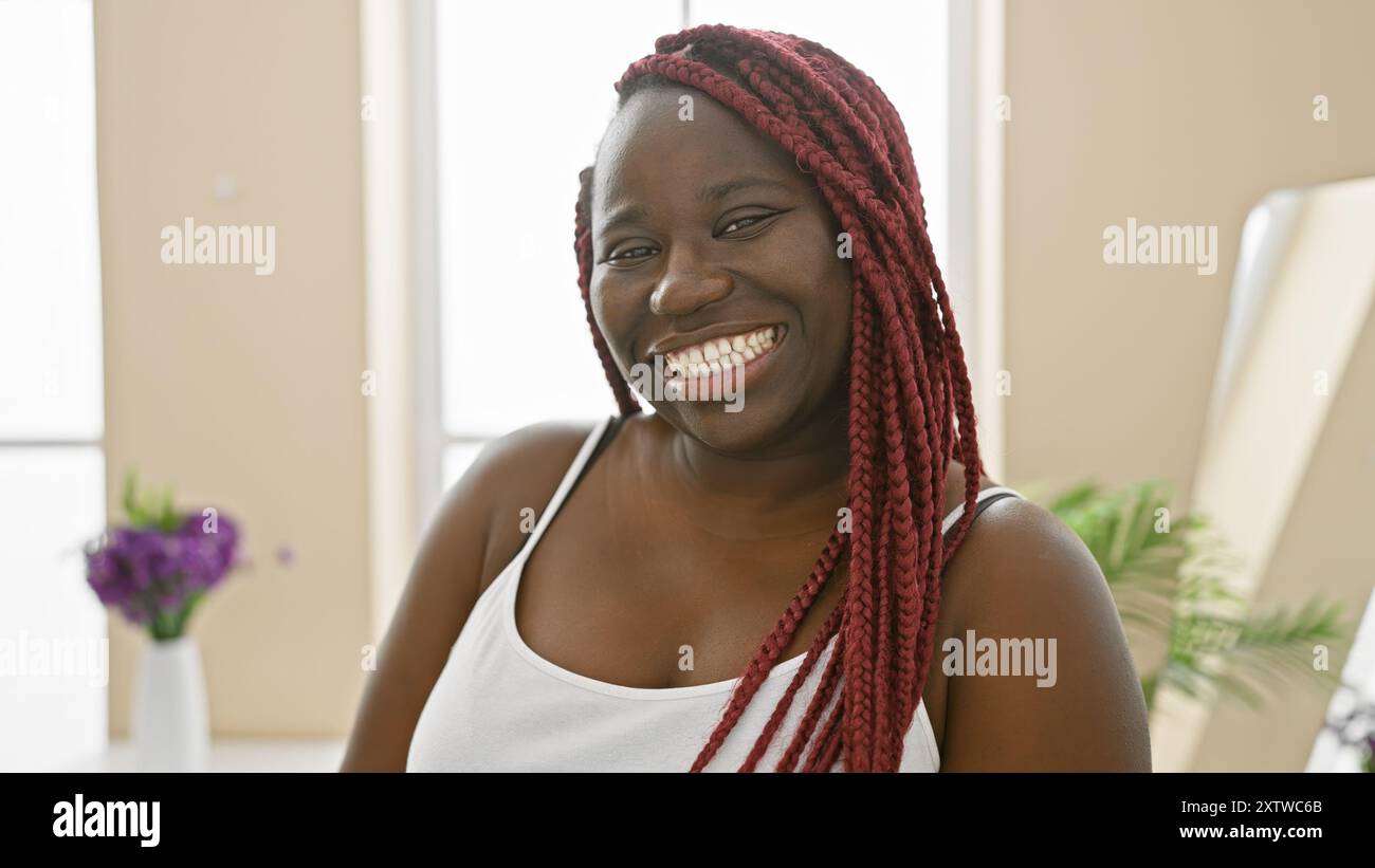 Portrait of a smiling black woman with red braids, indoors, at home in ...
