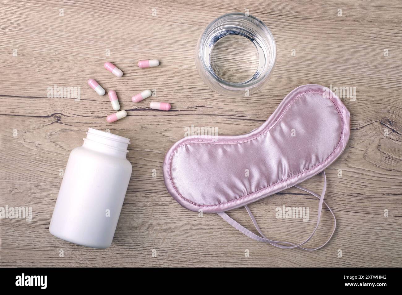 Pink eye mask next to a glas of water and sleeping pills on a table. Insomnia concept. Stock Photo