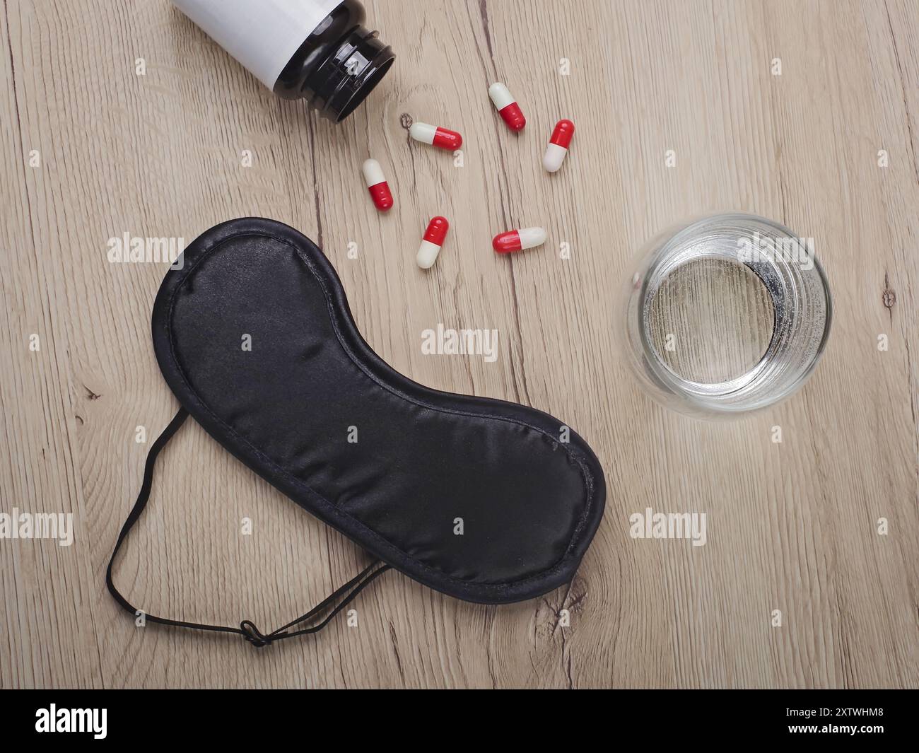 Black eye mask next to a glas of water and sleeping pills on a table. Insomnia concept. Stock Photo