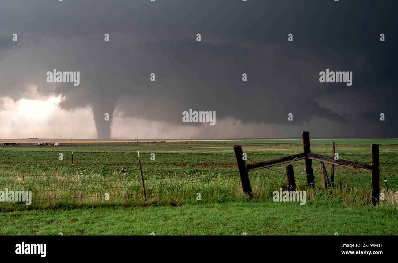 A tornado touches down in a rural landscape near a wooden fence under a ...