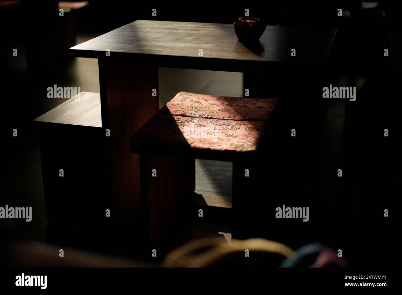 Sunlight filters through a window, casting a patterned shadow on a floral notebook resting on a dark wooden table. Stock Photo