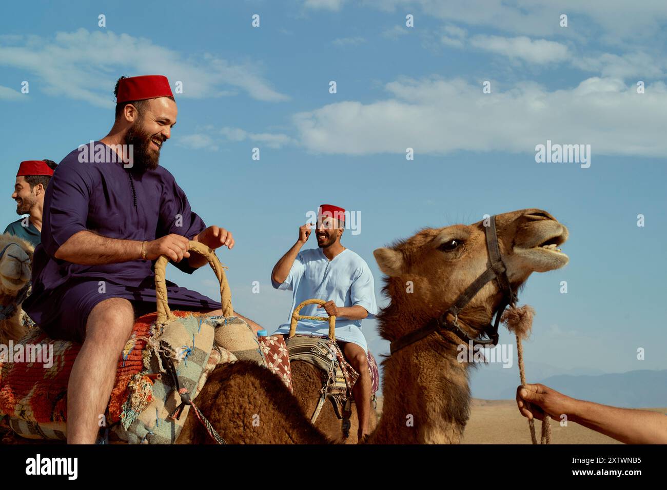 Traditional Camel Riding A group of men wearing traditional red hats smiling and riding camels ...