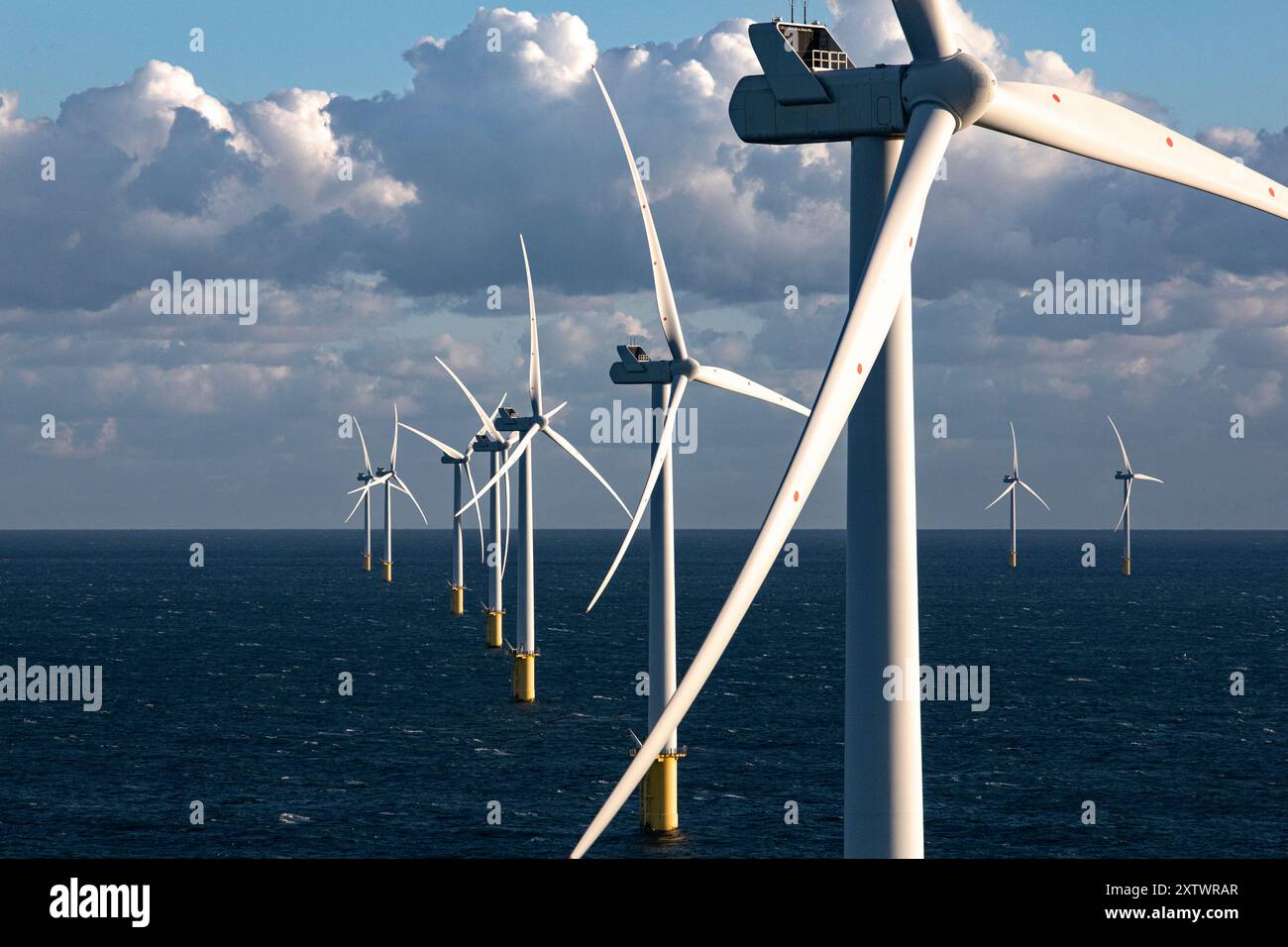 Offshore wind turbines stand tall above the ocean under a cloudy sky ...