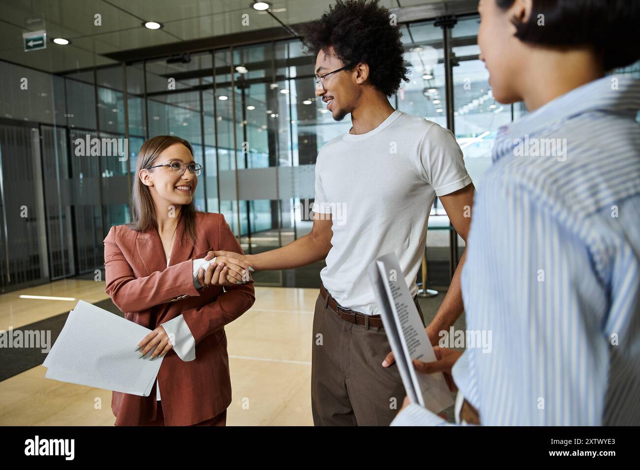 Three colleagues smile and chat in an office lobby. Stock Photo